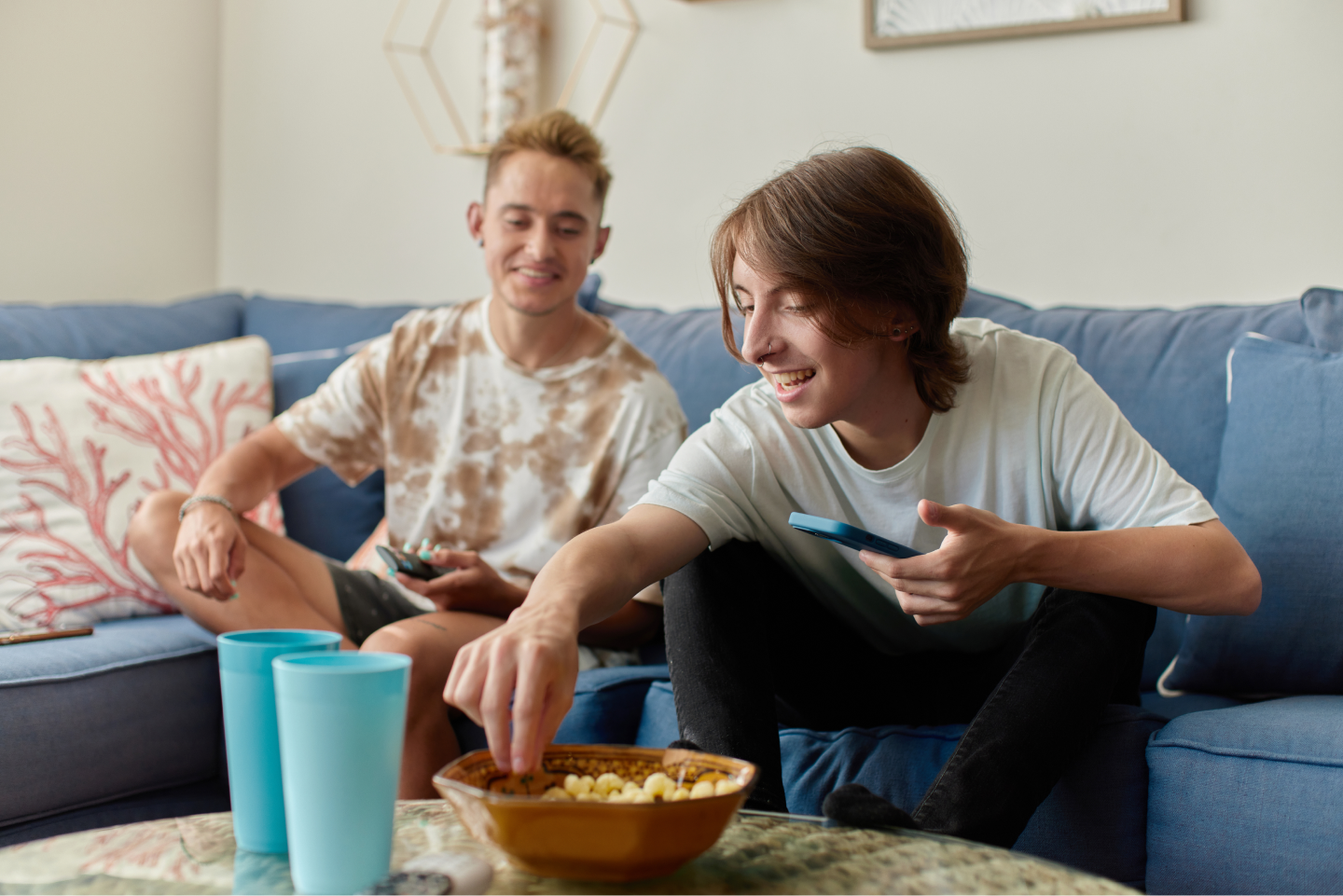 Two young men on their phones smiling sharing popcorn