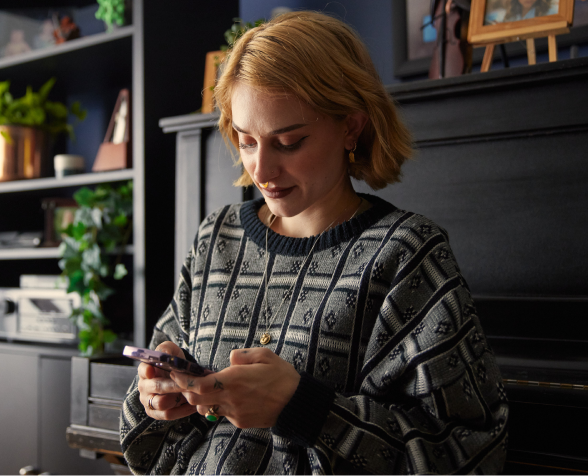 A young woman looking down at her smartphone in her home.