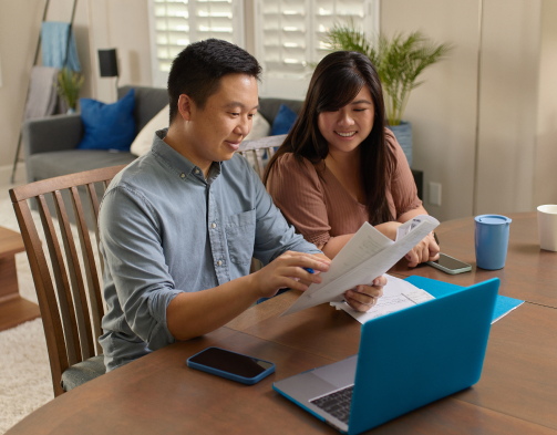 A man and a woman working with paperwork in their living room space.