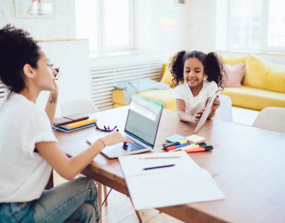 Une personne et un enfant assis à une table, avec des ordinateurs portables.