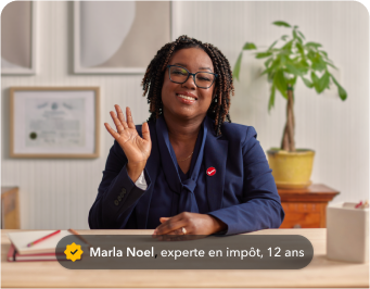 une photo de Marla, experte en impôt de TurboImpôt, assise à une table dans un bureau, souriant et faisant un signe de la main.