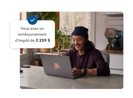 Un jeune homme sourit tout en travaillant sur son ordinateur portable chez lui. Illustration secondaire avec le texte et le crochet « Votre remboursement d’impôt est de 2 259 $ ».
