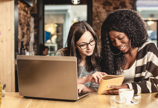 Two people sitting at a table with laptops.