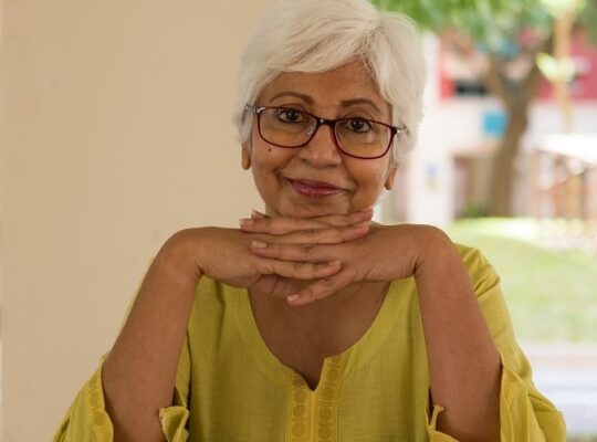 A person is smiling while she holds a glass.