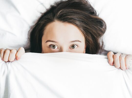 A person lies in bed with her head on her pillow.