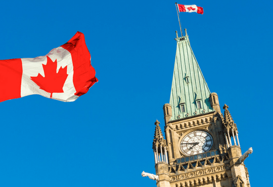 A Canadian flag flying in front of a clock. 