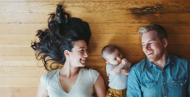 A person and a person are smiling while a baby looks on.