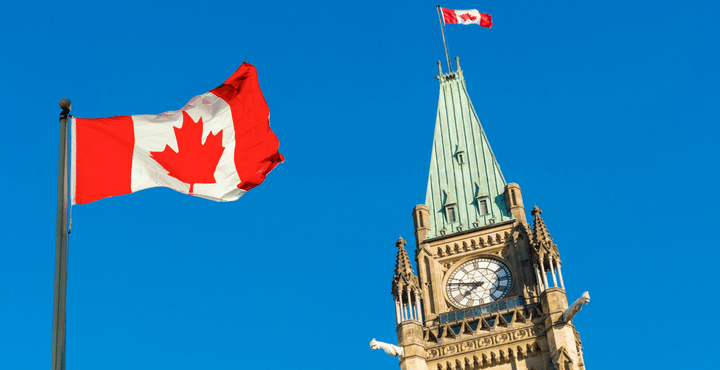 A Canadian flag flying in front of a clock. 