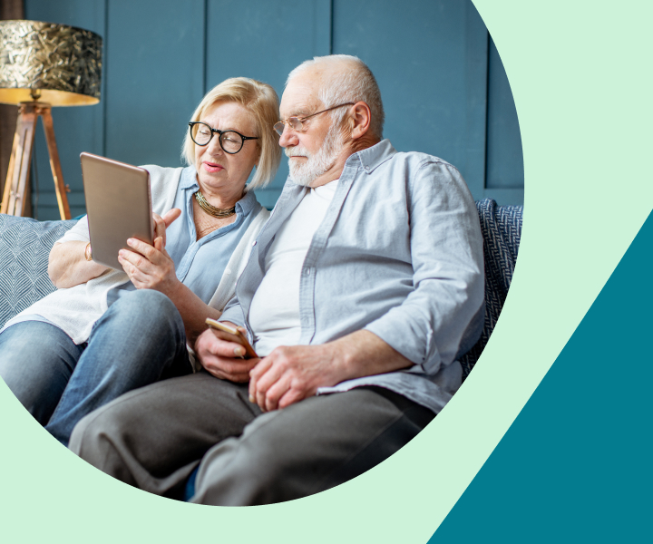 A couple is sitting on a couch and looking at a tablet.