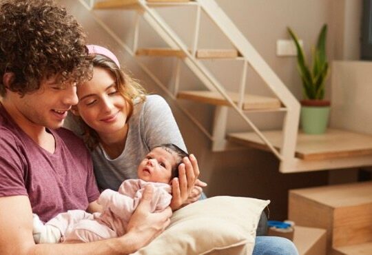 A person holding a baby while sitting on a bed.