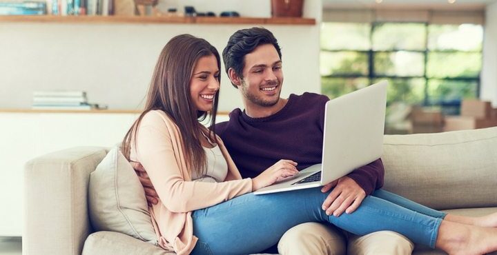 A person and person sitting on a couch looking at a laptop.