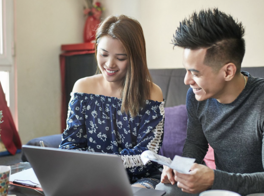 A person and person sitting on a couch looking at a laptop.