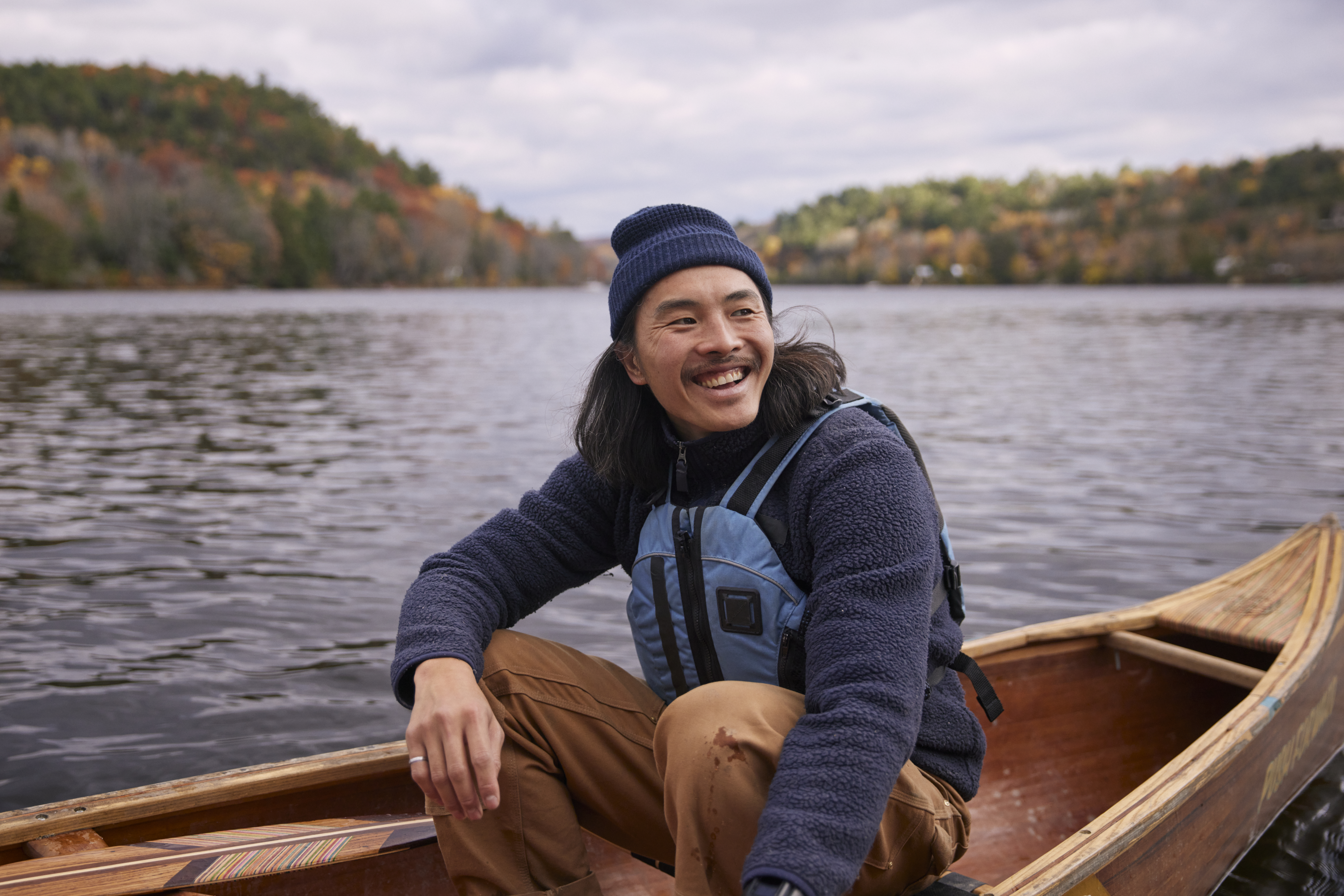 A person sitting on a boat smiling while wearing a hat.