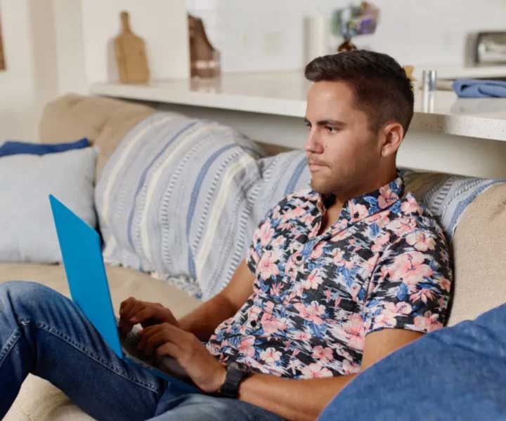 A person is working on a laptop while sitting on a couch.