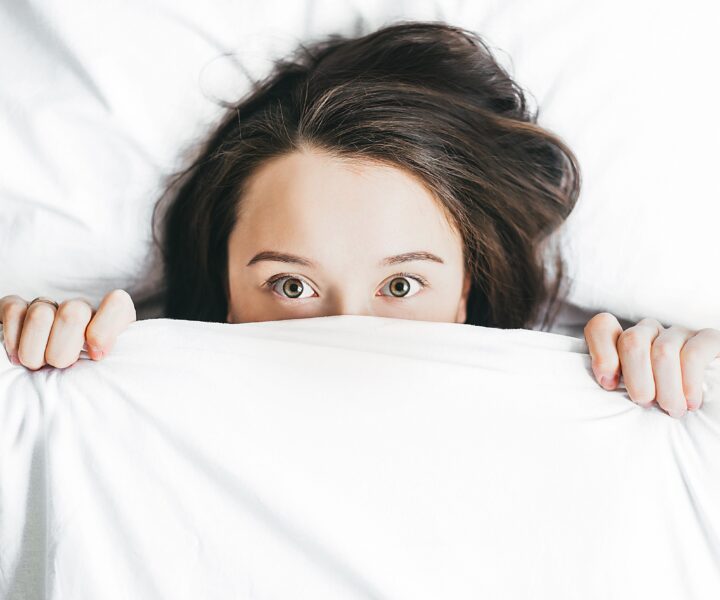 A person lies in bed with her head on her pillow.