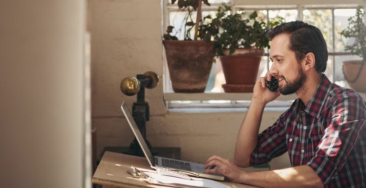 A person sitting at a table with a laptop and a cell phone.