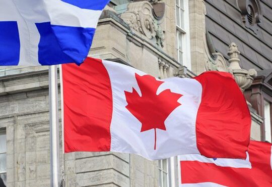 A Canadian flag flying in front of a blue building.