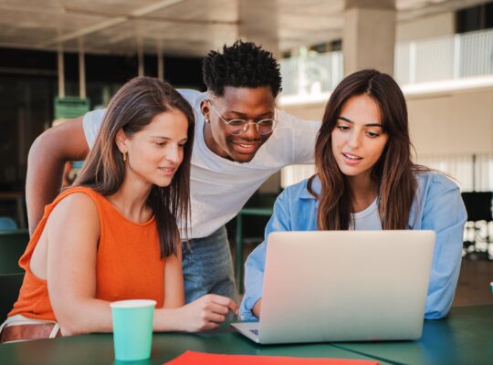 Three people sitting at a table with laptops.