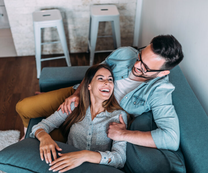 A person and person sitting on a couch smiling.