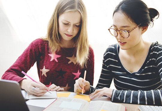 Two people are writing on paper with pens and pencils.