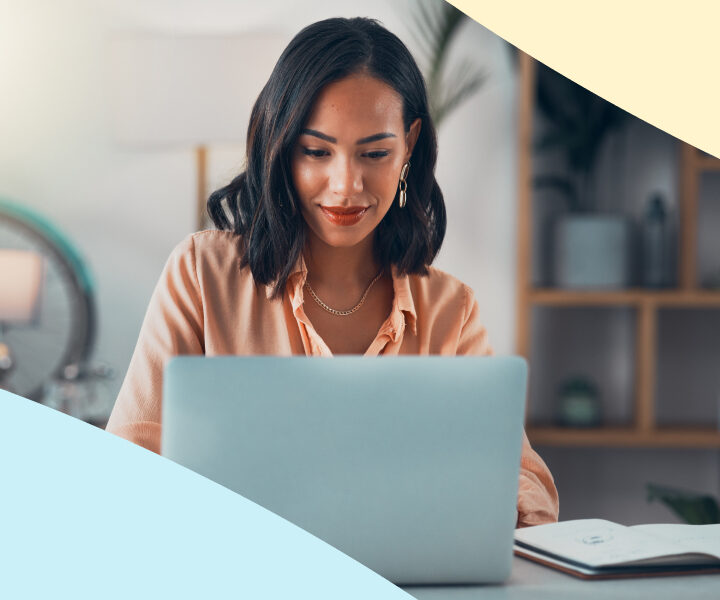 A woman is smiling while working on a laptop.