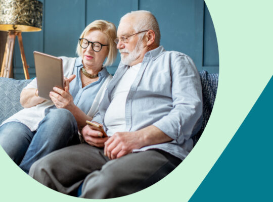 A couple is sitting on a couch and looking at a tablet.