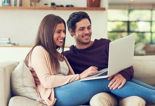 A person and person sitting on a couch looking at a laptop.