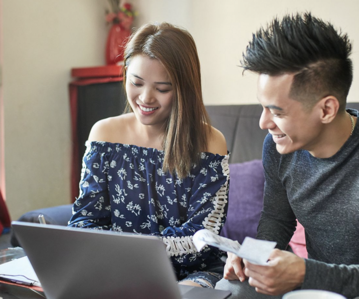 A person and person sitting on a couch looking at a laptop.