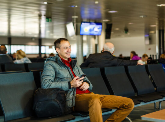 A person sitting on a bench with a bag of luggage.