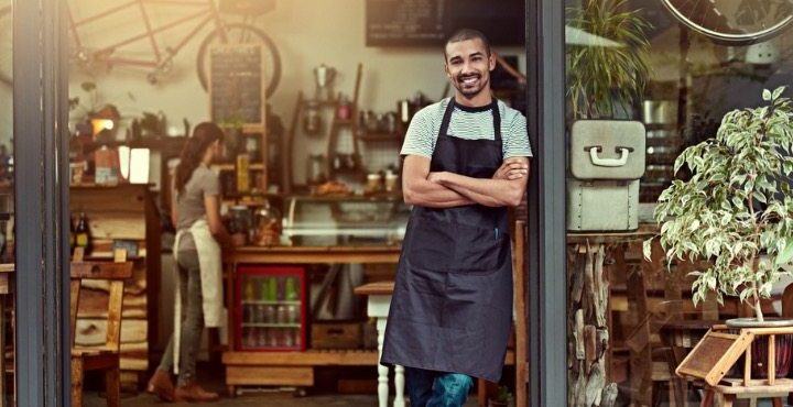 A person smiling and standing in a cafe.