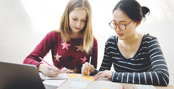 Two people are writing on paper with pens and pencils.