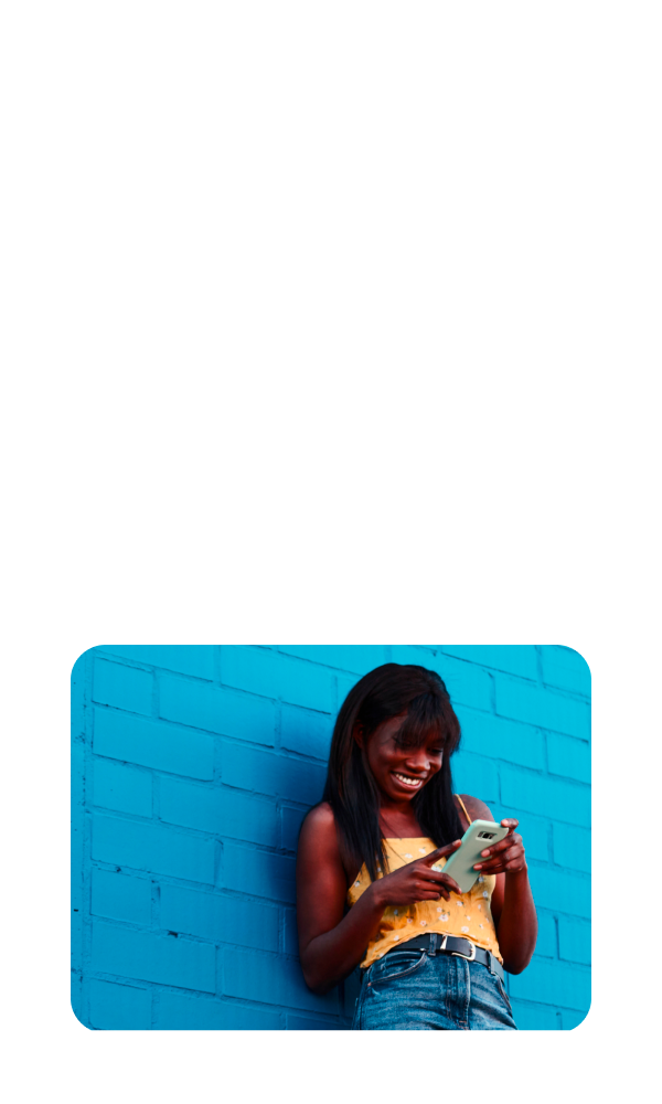 A smiling young woman casually  leans against a wall while looking at her tax return on her smartphone