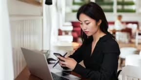 A woman at her desk with a phone and a laptop.