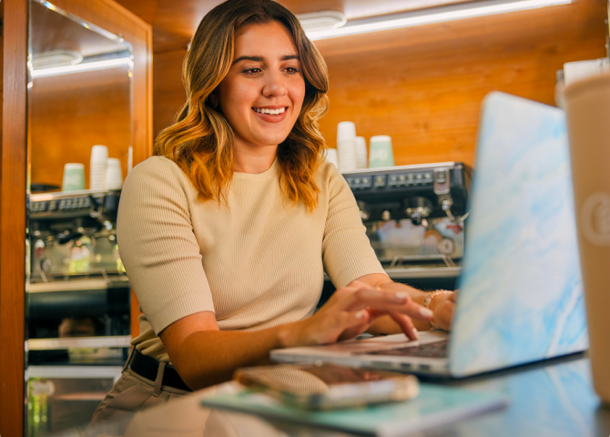 TurboTax customer Carina is smiling as she looks down at her laptop on the table.