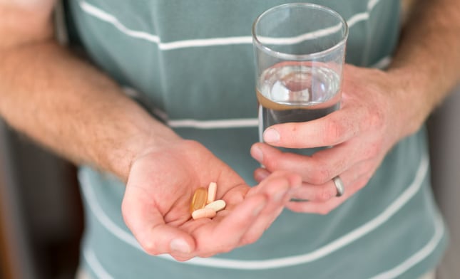 young man holding a glass of water in one hand and pills in the other