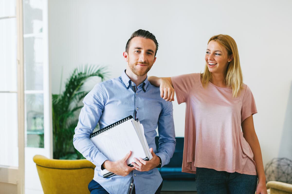 A smiling woman leans with her elbow on the shoulder of her male coworker