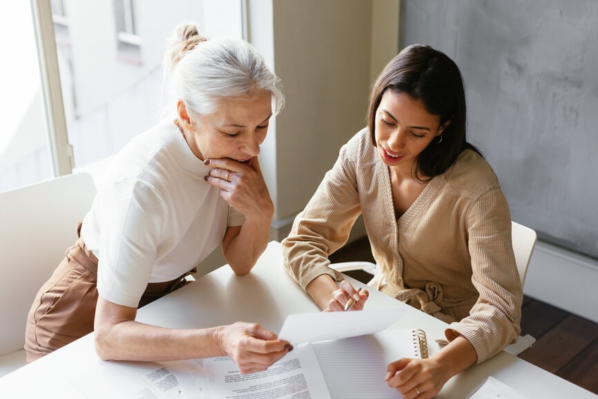 Two business women at a desk looking over paperwork to find out how to lower their taxable income.