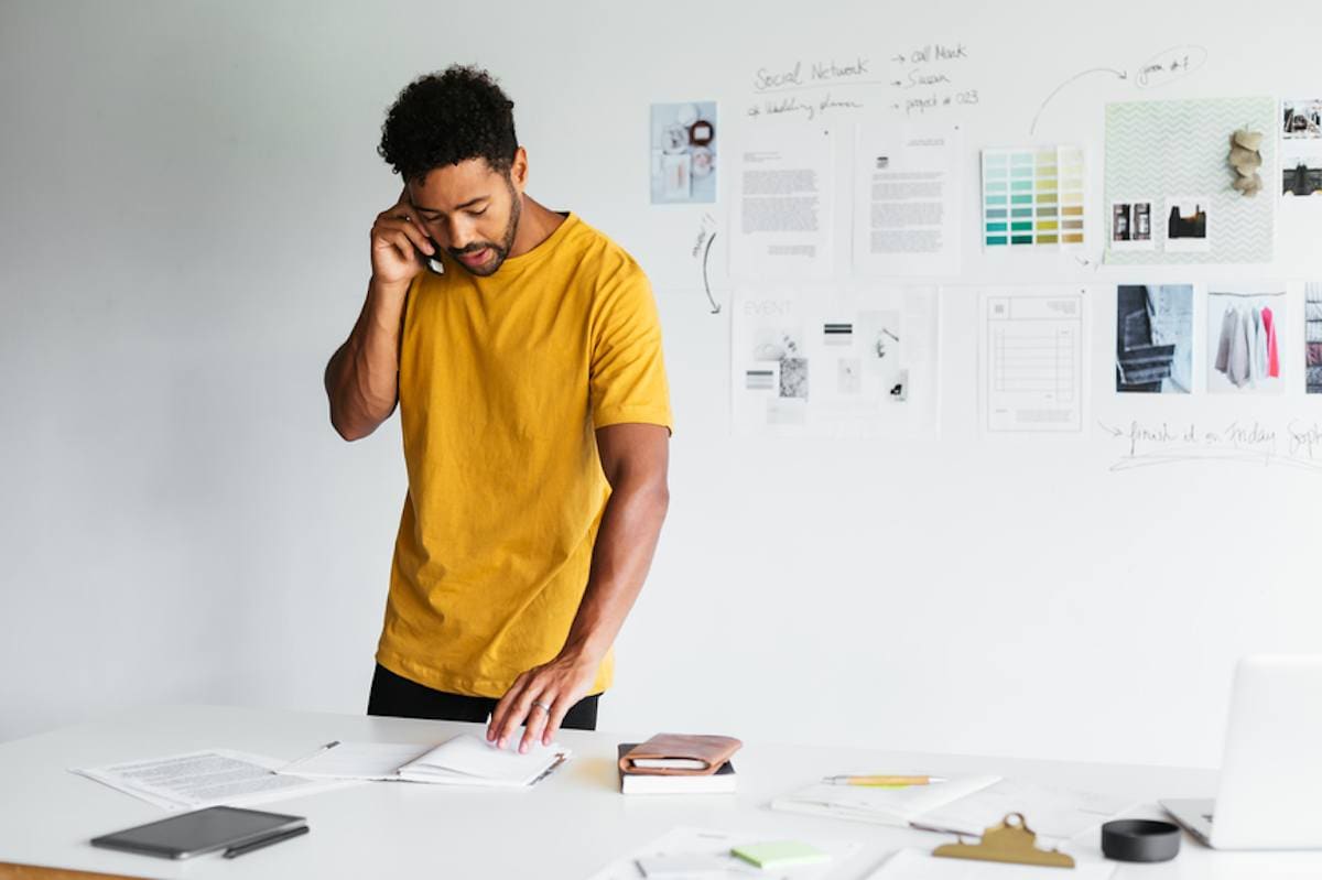 Male event planner speaks on cell phone and checks notes in office