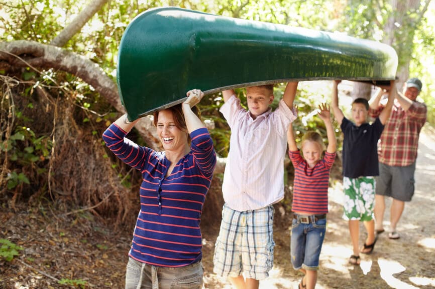 Happy family of five carrying a canoe over their heads on the way to the lake.