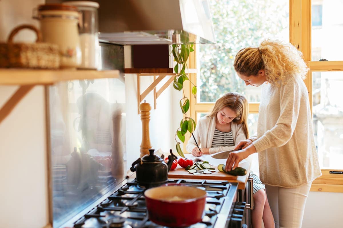 A mother and her young daughter prepare food together in their kitchen.