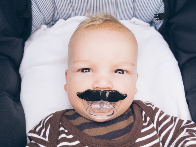 Baby with a pacifier shaped like a mustache.