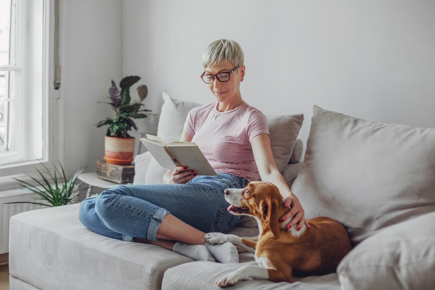 Woman reading on the couch with her dog.
