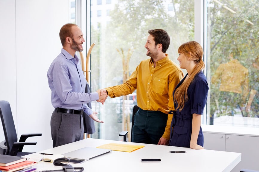 A young couple shaking hands with a tax professional in his office.