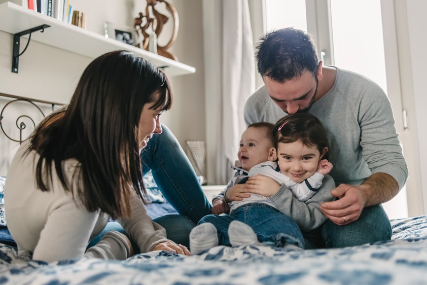 Parents, a baby, and a toddler sit on a bed