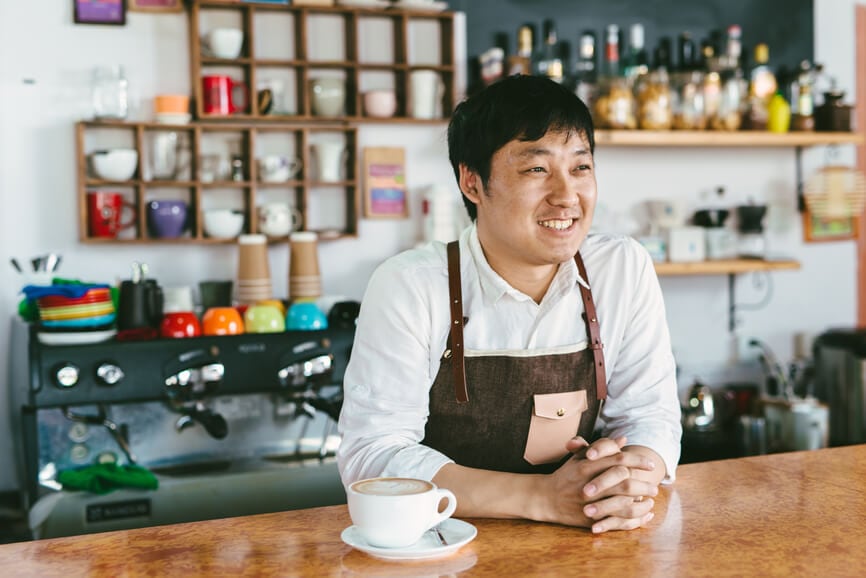 Barista at a coffee shop leaning over the counter and smiling.