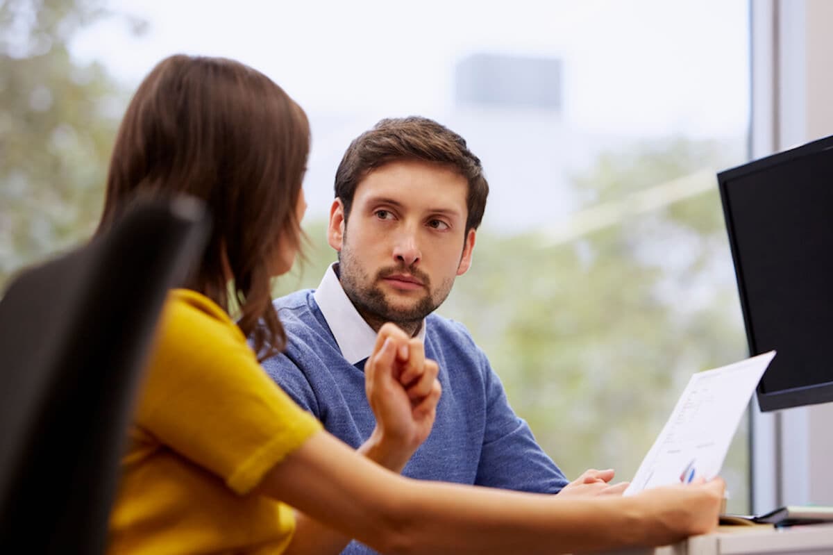 A man and a woman discuss business documents by a window in an office