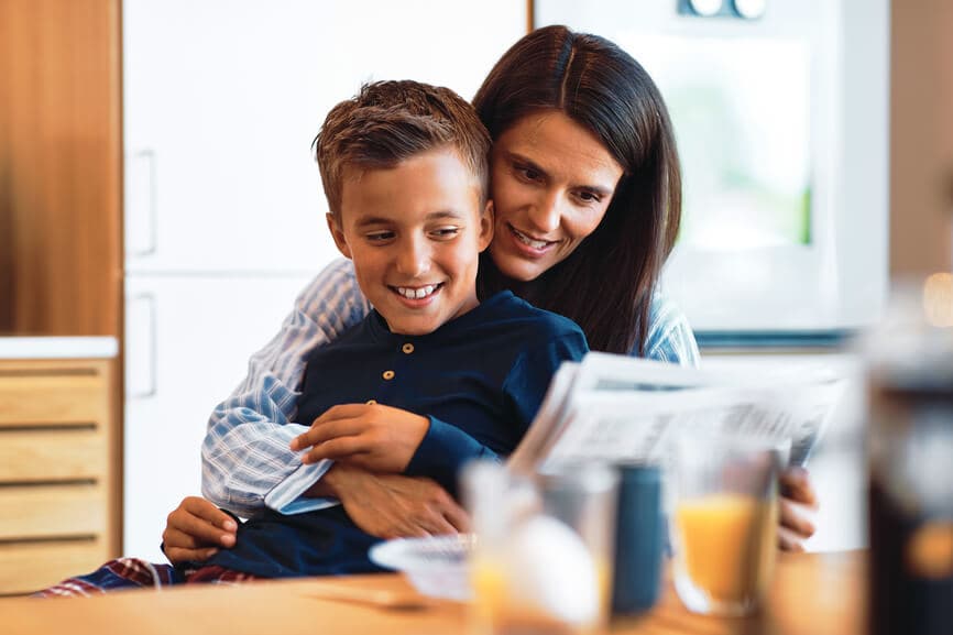 Woman holding her son while reading the newspaper in the morning.