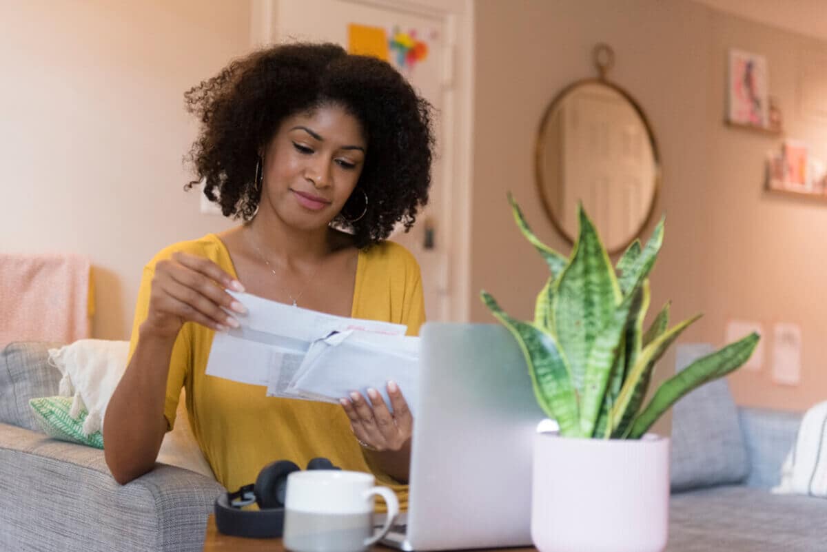 A Black woman sits at a desk in front of a laptop and looks through documents.