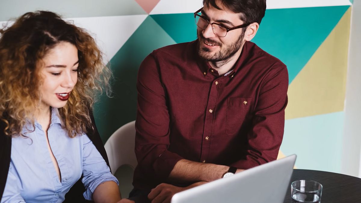 young woman working on laptop as a young man looks on