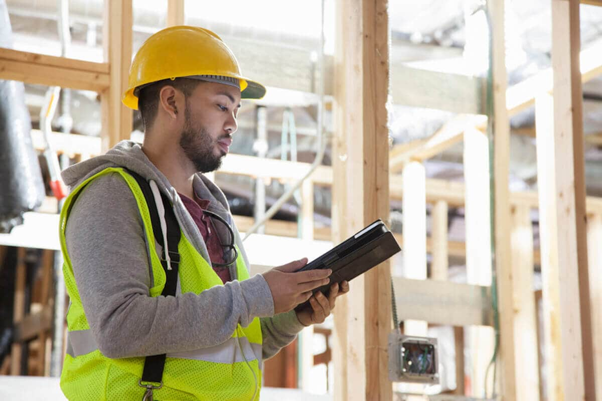 Construction worker in hard hat checks his notebook computer inside building under construction